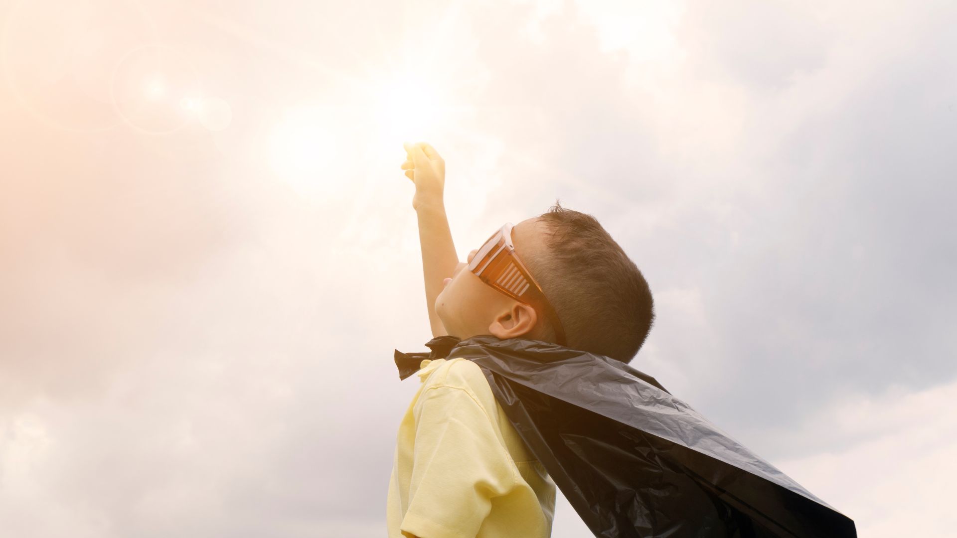 一個穿著超級英雄斗篷的小男孩正伸向太陽，展現決心和勇敢。